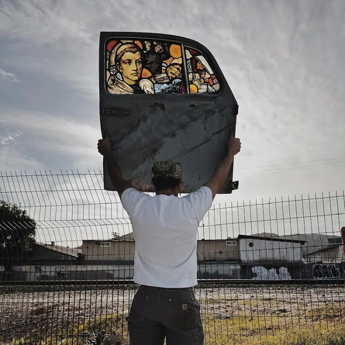 Artist holding a burned and rusted Porsche 911 door turned into a stained-glass sculpture.