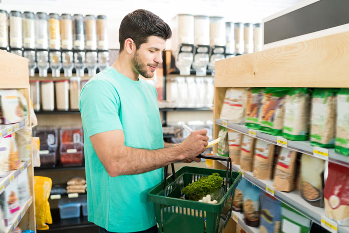 A man in a grocery store checking a list while holding a basket, possibly facing issues that lead to a divorce lawyer.