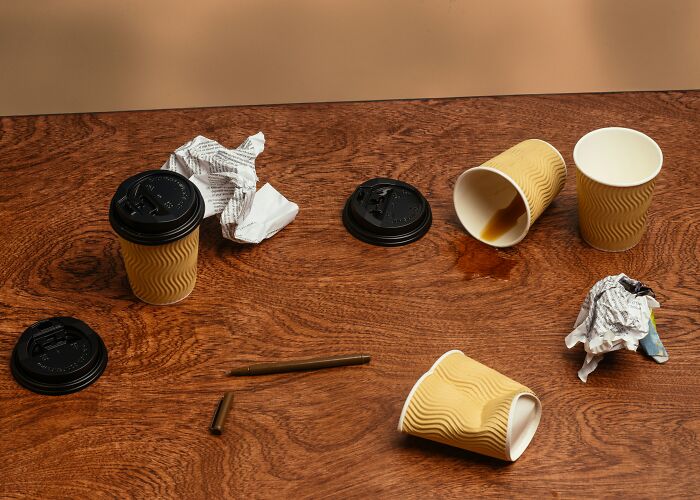 Spilled coffee cups, crumpled paper, and a broken pen on a wooden table, symbolizing a messy situation that could lead to being fired.