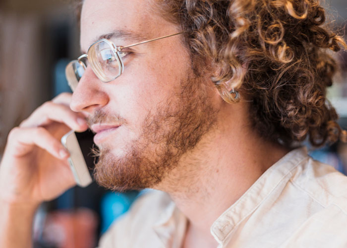 A man with curly hair and glasses talking on a phone. This image can be used for boss stories that make you quit your job.