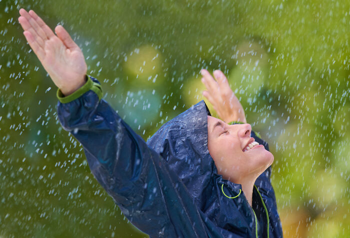 A person in a blue rain jacket with arms raised, enjoying the rain, reflecting interesting facts about weather.