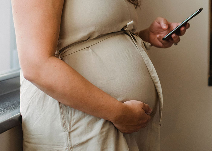 A pregnant woman holds her belly, contemplating feelings of loneliness as birthdays approach.