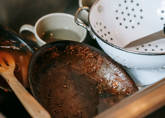 A pile of dirty dishes in a sink, showing women's experiences visiting a man's home for the first time.