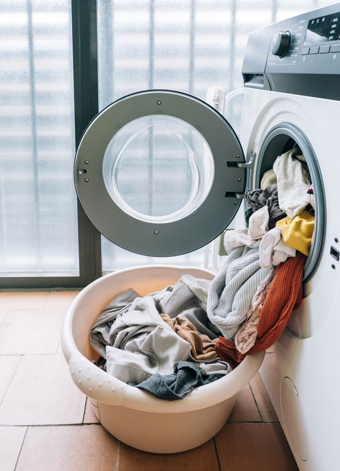 A washing machine overflowing with laundry next to a basket, depicting domestic tasks that might be men's complaints.