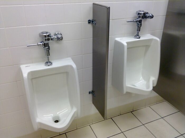 Two urinals in a public bathroom, one with a missing divider, creating an awkward public horror story scenario.