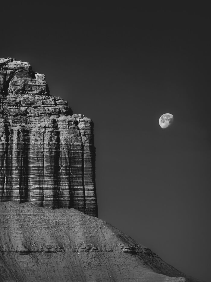A stark black and white iPhone photography awards winning photo of a rugged mountain peak with a full moon.
