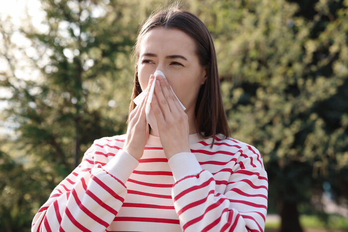 A woman sneezing into a tissue outdoors, depicting interesting facts related to health and human body.