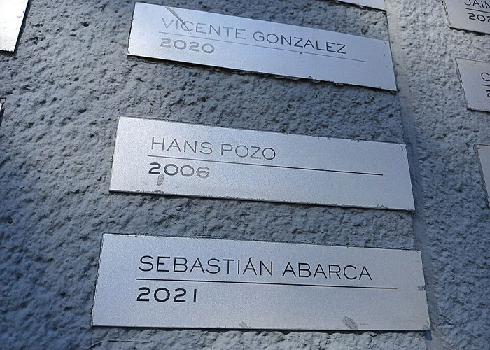 Metal plaques on a wall, listing names and years: Vicente Gonzalez 2020, Hans Pozo 2006, Sebastian Abarca 2021, part of a man's horrific fate.