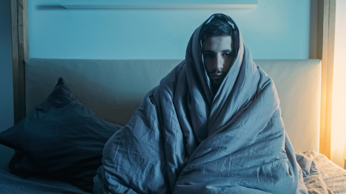 A man wrapped in a blanket in bed, looking disturbed, representing creepy and mysterious things that happened to people.