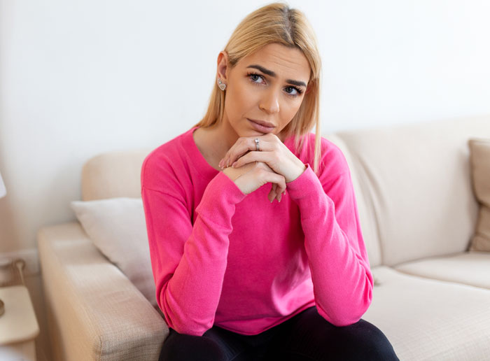 A blonde woman sitting on a couch with a sad expression. Hard truths women learned.