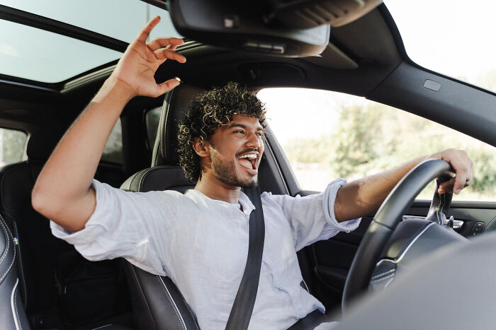 A man driving with his hands up, happily singing, thankful to not have any pocket dial stories.