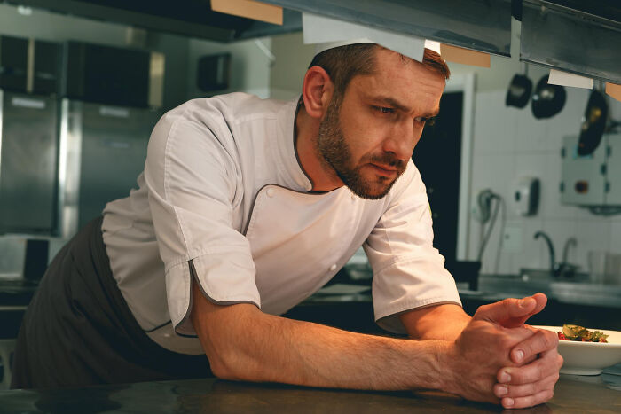 A male chef in uniform, looking thoughtful and leaning on a counter. One of the dumbest reasons people got fired.