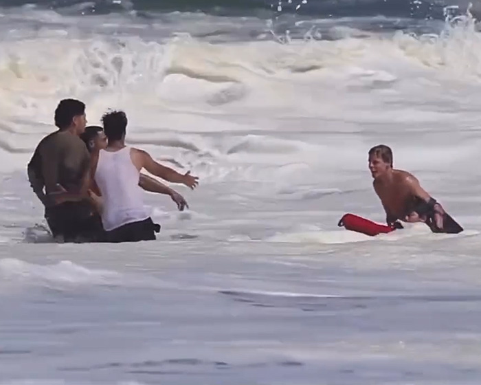 A 16-year-old lifeguard with a rescue tube assists a person in the ocean, with others approaching. A 16-year-old lifeguard with a rescue tube assists a person in the ocean, with others approaching.