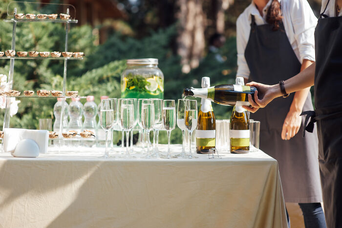 Champagne being poured into glasses at an outdoor wedding reception with appetizers on a tiered tray.