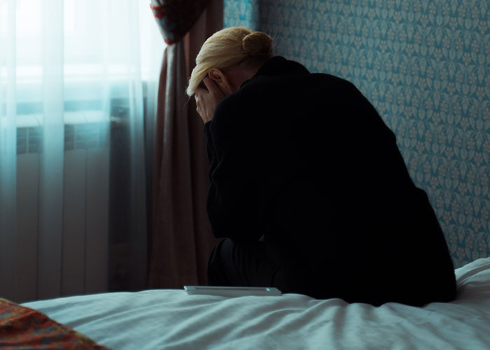 A woman sits on a bed, head in hands, experiencing loneliness and not looking forward to birthdays.