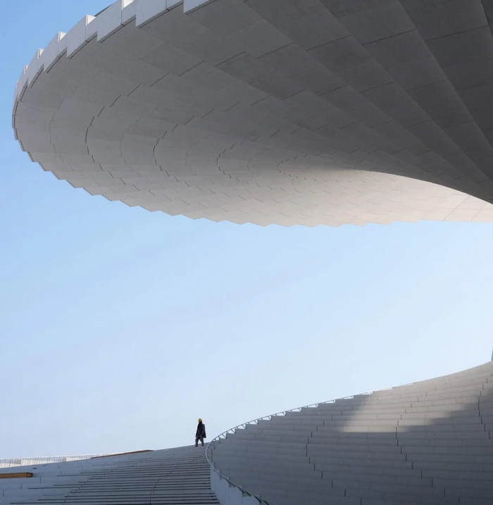 A person ascending a grand, curved staircase of a striking modern architecture design under a clear blue sky.