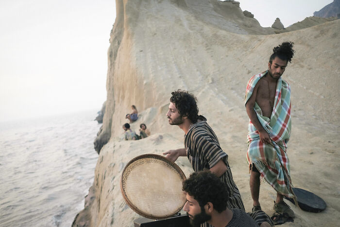 Men on a rocky cliffside overlooking the sea, playing traditional music, highlighting the human side of the Strait of Hormuz.