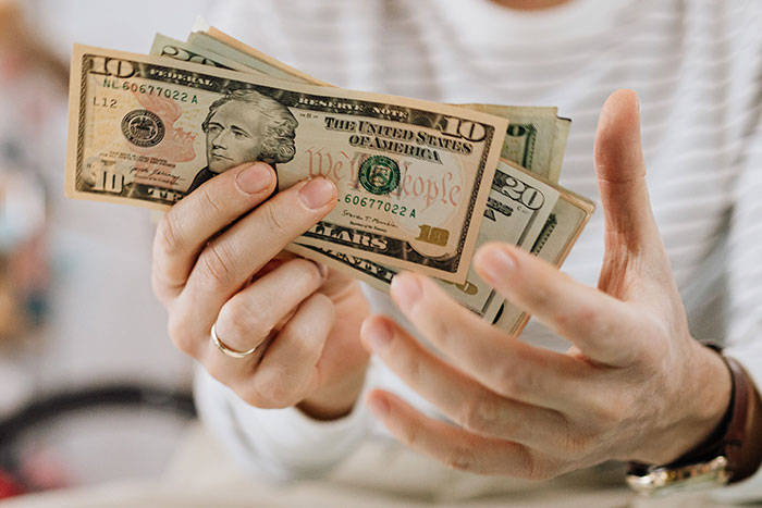 Hands holding various dollar bills, suggesting financial implications for parents of kids with unfortunate names.