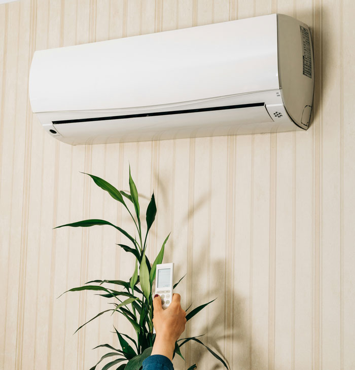 A hand points a remote control at an air conditioner, one of many affordable things that were once only for the rich.