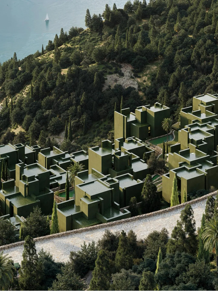 Unique modern architecture designs of green buildings nestled on a hillside overlooking a body of water with a sailboat.