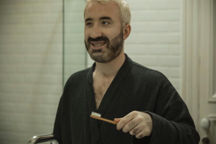 A man in a robe holds a toothbrush, contemplating unhygienic choices.