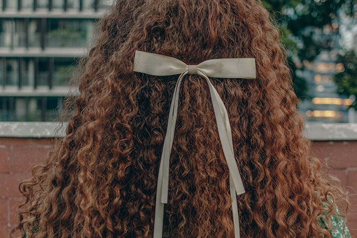 The back of a woman's head with curly brown hair and a white bow, relating to kids with unfortunate names.