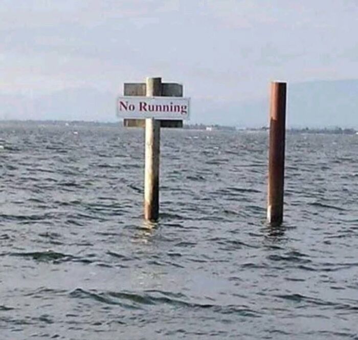 A 'No Running' sign submerged in deep water, humorously highlighting America's cultural decline into idiocy.