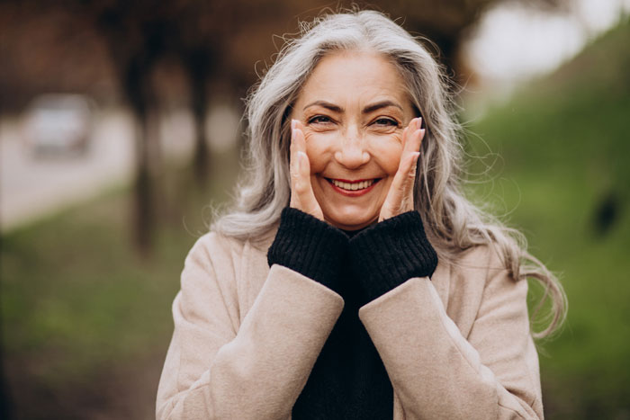 A happy older woman with long gray hair smiling, sharing truths women learned.