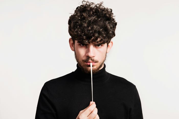 A man with curly hair and beard holds a cotton swab in front of his mouth, depicting unhygienic situations.