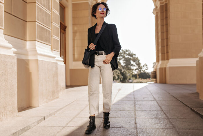 A stylish woman in a black blazer and light pants, walking outdoors, showcasing fashion trends and items.