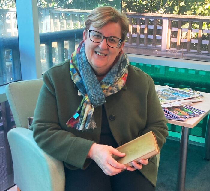 A smiling woman holding a book, showcasing interesting posts that an Aussie might fully understand.