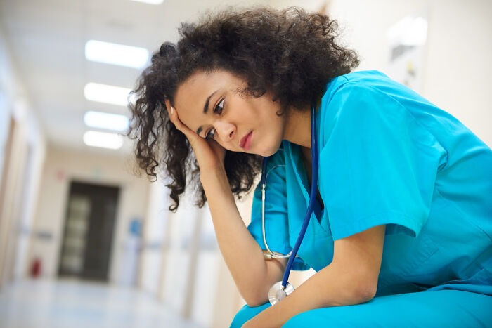 Sad medical professional sitting in a hospital hallway, reflecting on the medical industry.