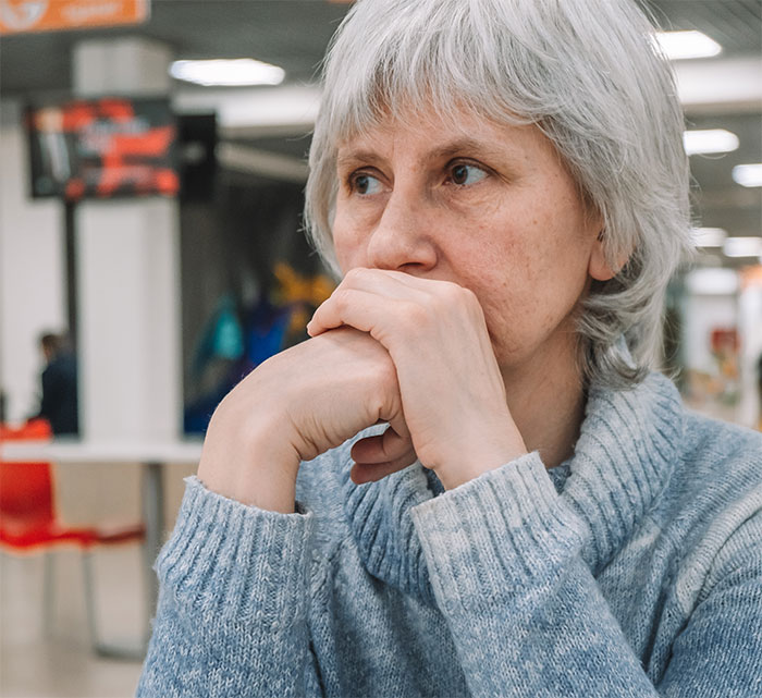 A woman with short grey hair and a blue sweater, looking away thoughtfully, portraying defeat after xenophobic remarks. A woman with short grey hair and a blue sweater, looking away thoughtfully, portraying defeat after xenophobic remarks.