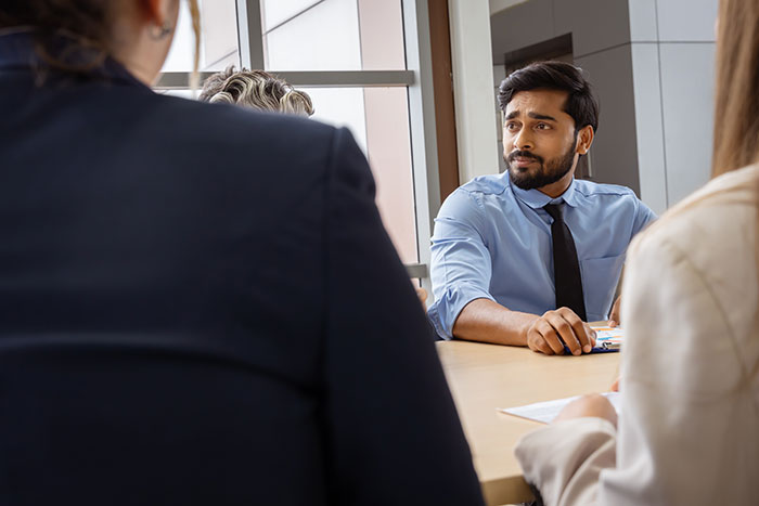 A software engineer looks worried during a meeting, discussing a new hiring scam.