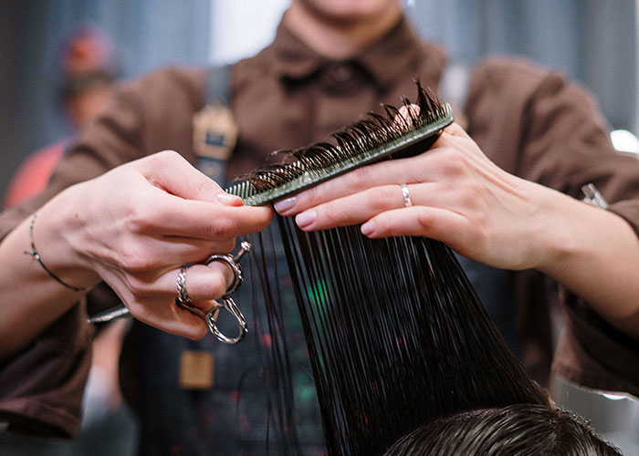 Hairdresser hands with scissors and comb, cutting wet dark hair, representing the act of getting used.