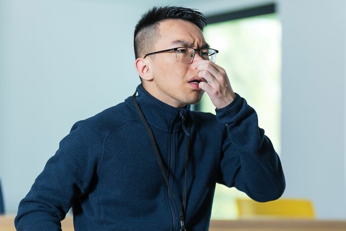 A man with glasses pinches his nose, reacting to an unpleasant smell. Stories of people got fired for bad behavior.