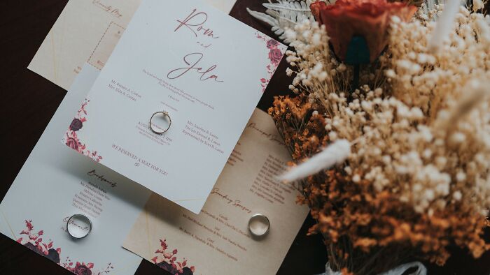 Wedding invitations with a floral design and a gold ring, lying next to a dried flower bouquet, symbolizing new family pictures.