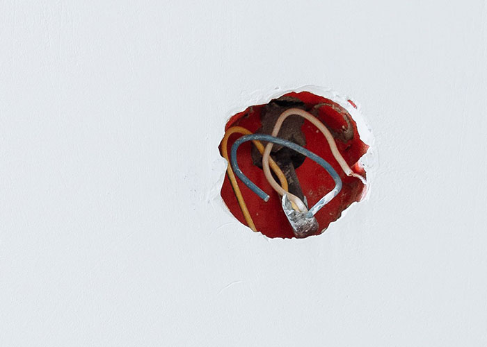 Exposed electrical wires in a hole in a wall, suggesting an unsafe condition in a man's home.