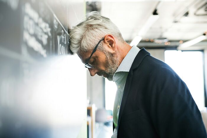 A stressed teacher leaning against a blackboard, embodying the grim picture teachers paint of Gen Alpha's school life.