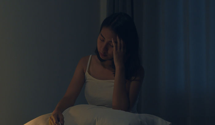 A woman sits in a dimly lit room, holding her head, reflecting the sentiment of men's complaints.
