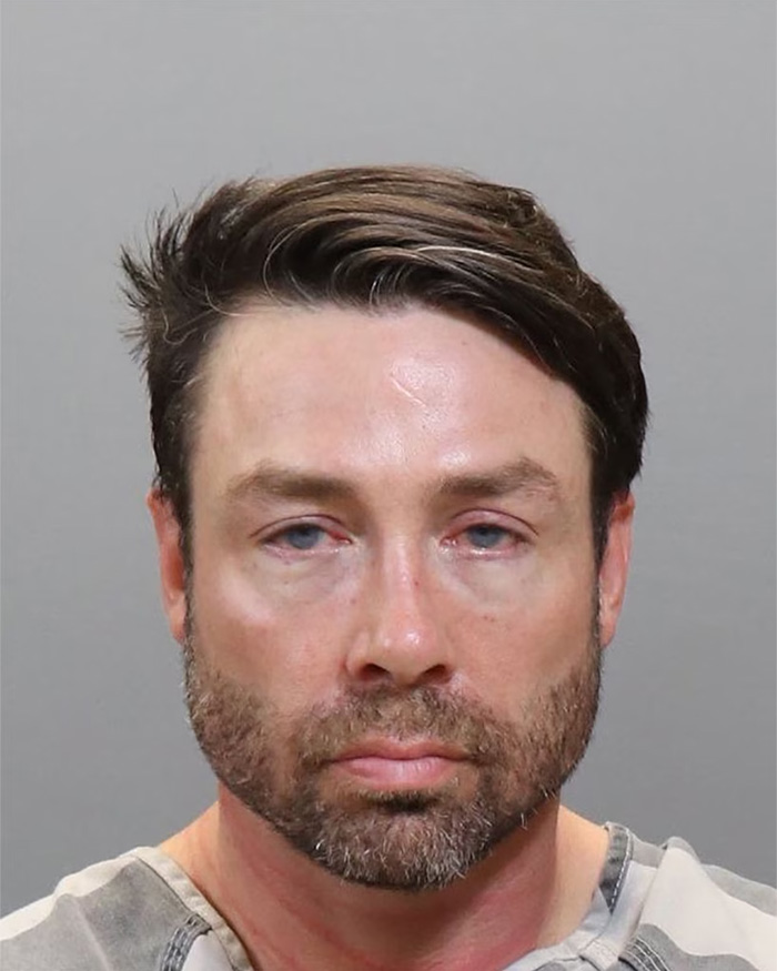Mugshot of a reality star with a beard and patterned shirt, associated with serious crimes.
