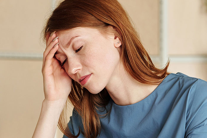 A woman with red hair looking stressed, holding her head, related to kids with unfortunate names.
