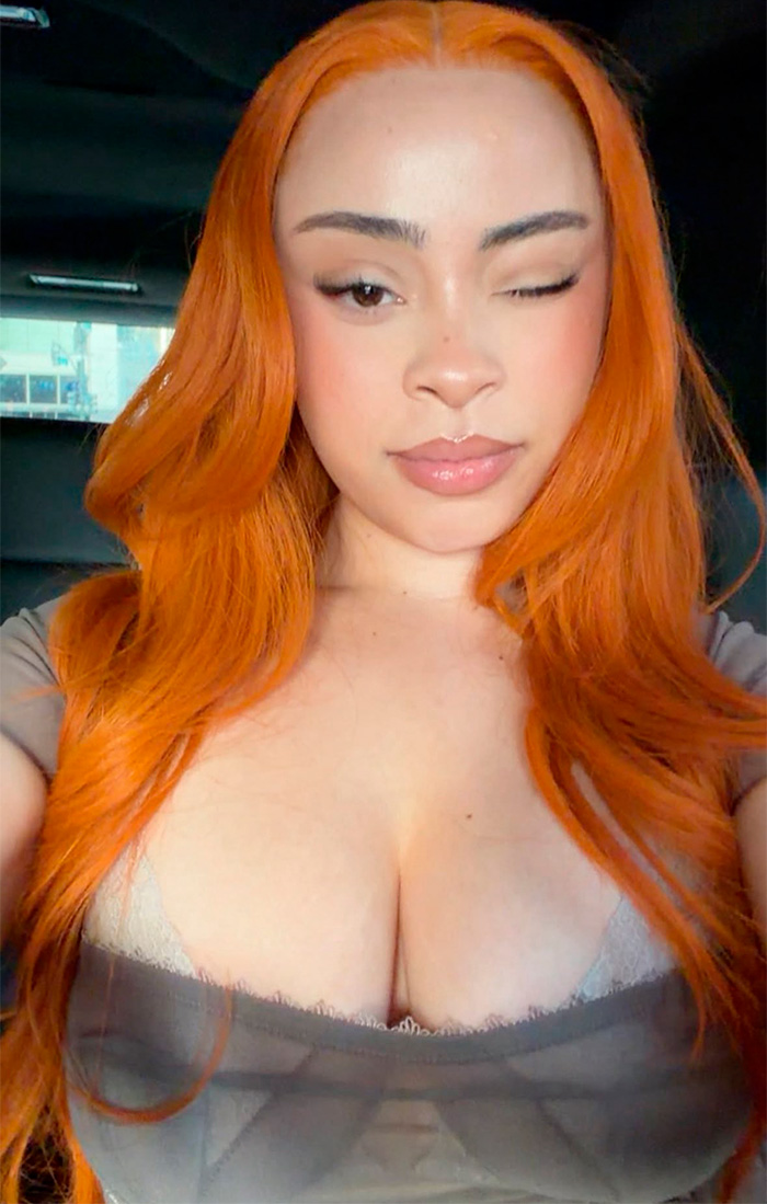 A woman with bright orange hair winks, showing a fashion moment. This look could be one of the worst-dressed celebrities at Taylor Swift's wedding.