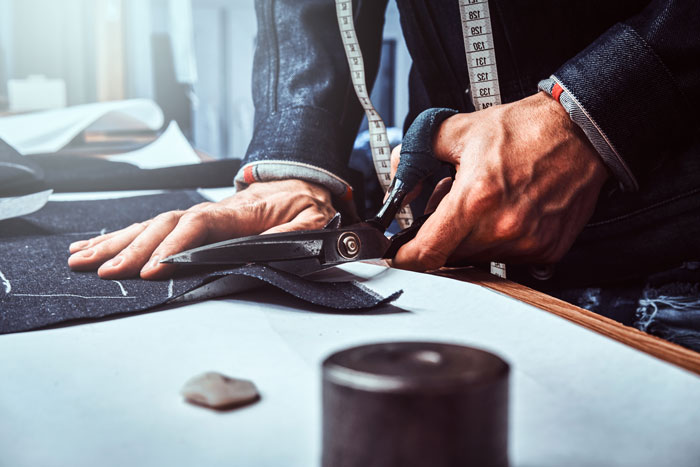 A tailor cutting fabric with scissors, showcasing custom clothing as surprisingly affordable.