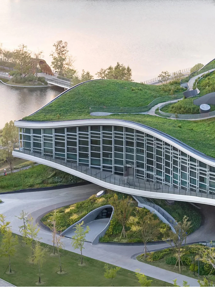 Modern architecture design featuring a building with a green roof, blending into the natural landscape beside a lake.