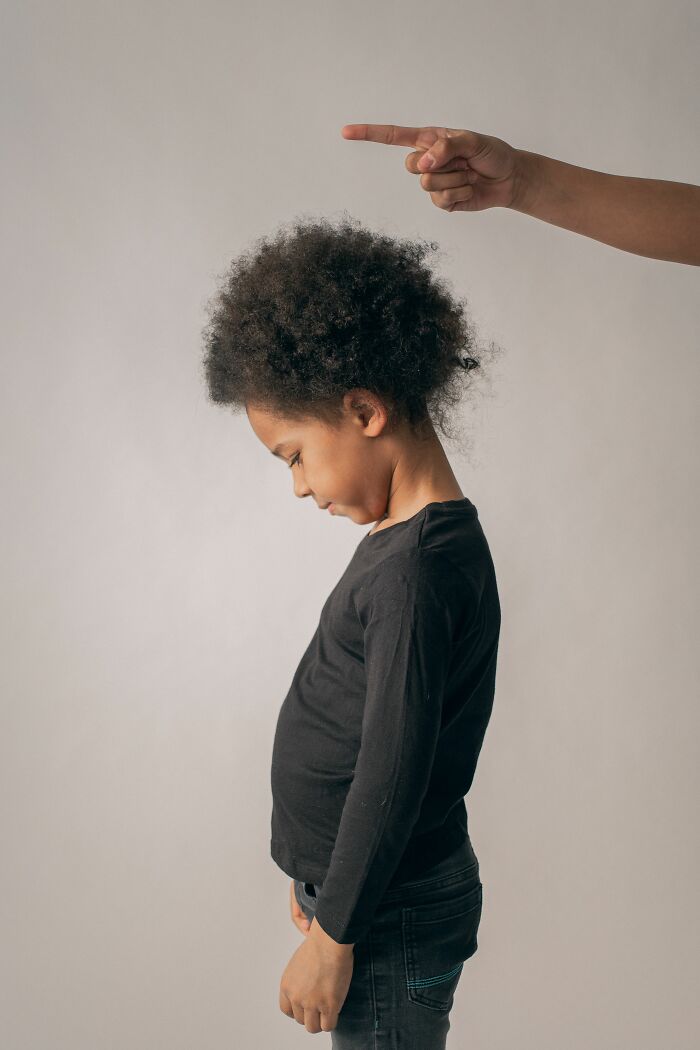 Parent pointing at sad child with curly hair in black shirt