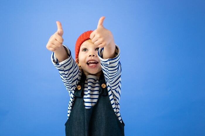 Happy child showing thumbs up wearing red hat and striped shirt