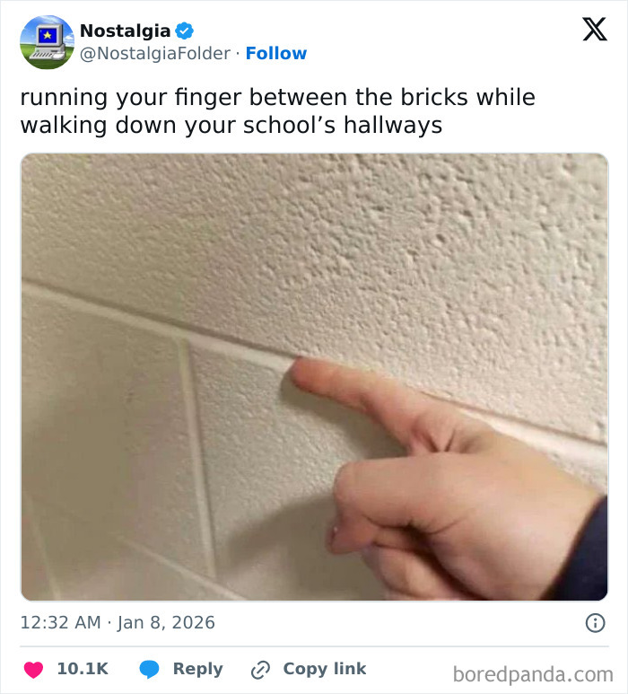 A finger runs along the grout line between textured bricks in a school hallway, evoking nostalgia.