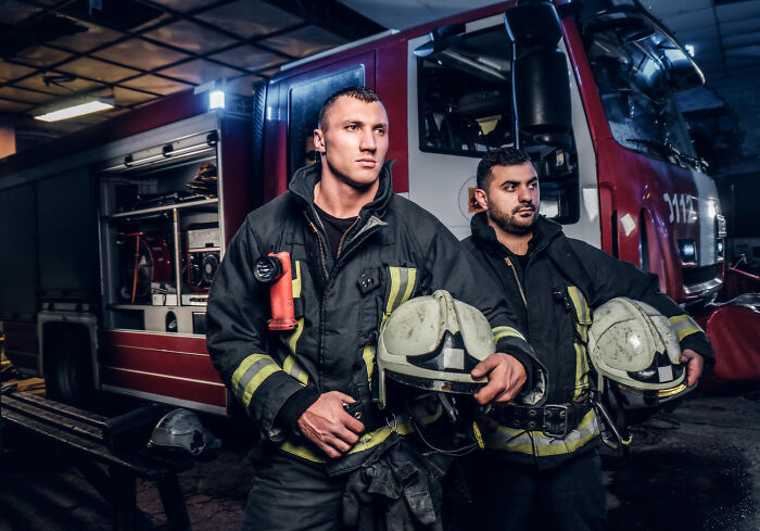 Two firefighters in protective gear standing in front of a fire truck, representing jobs that make women swipe left.