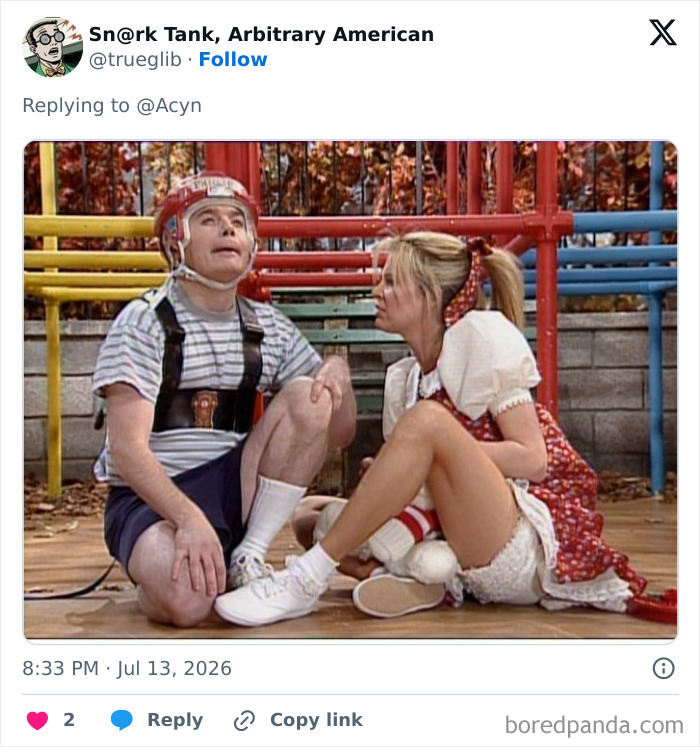 A man wearing a red special helmet in a playground, looking up, with a woman beside him, part of the instant mockery.